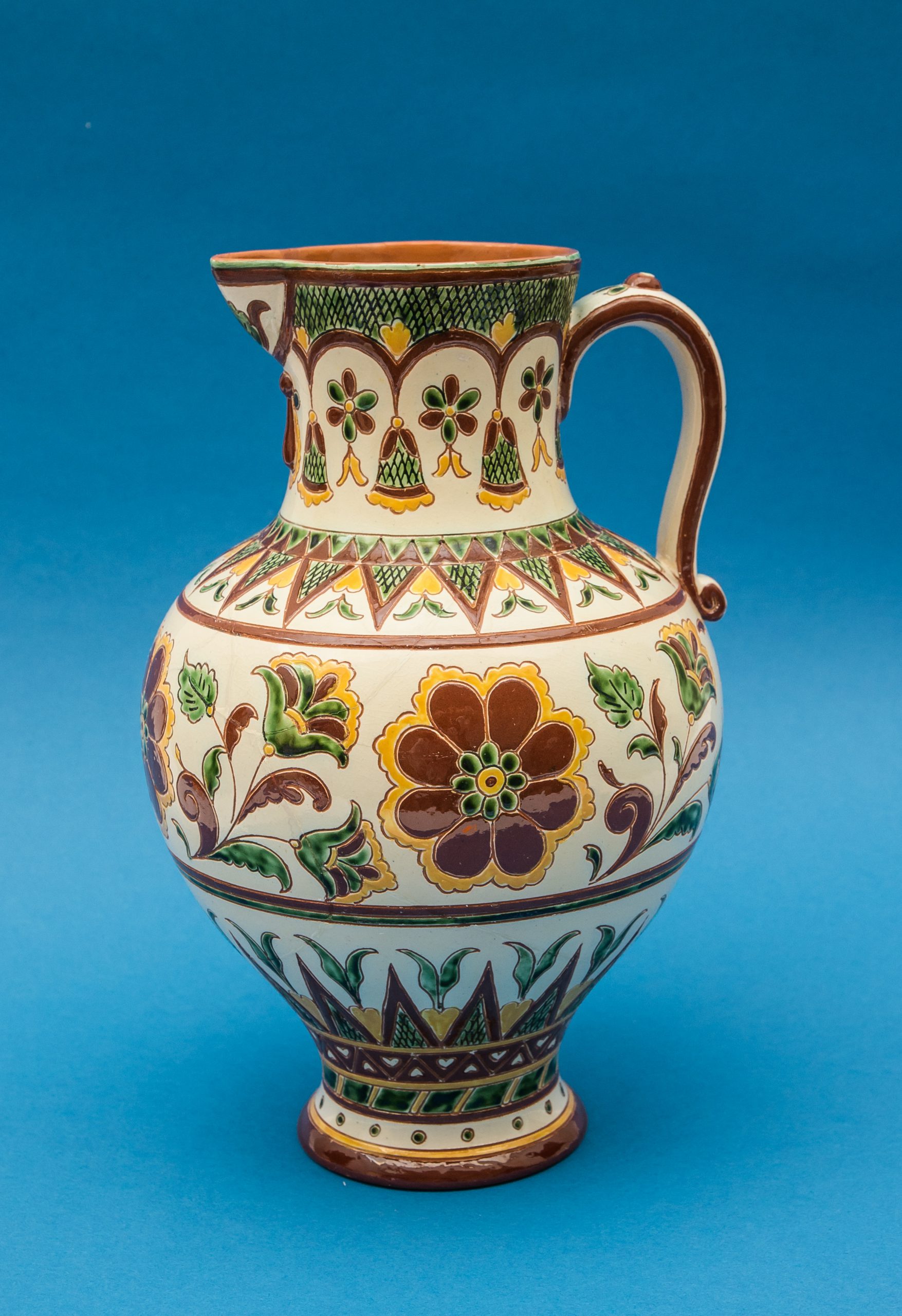 Hand-painted ceramic jug with a floral ornament on a blue background.
