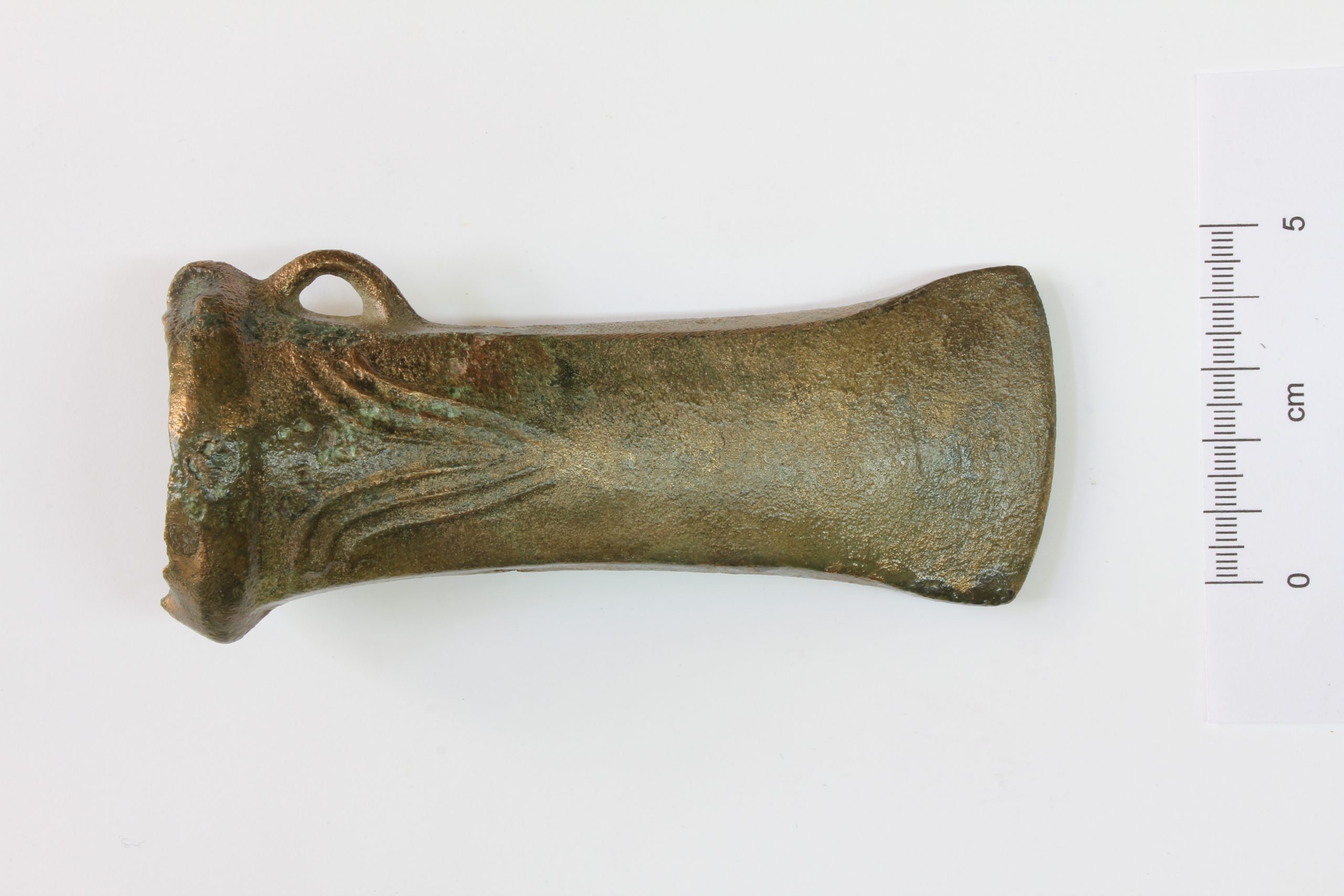 A bronze axe from the Bronze Age with a mounting eyelet, shown from the side against a white background with a centimeter scale.