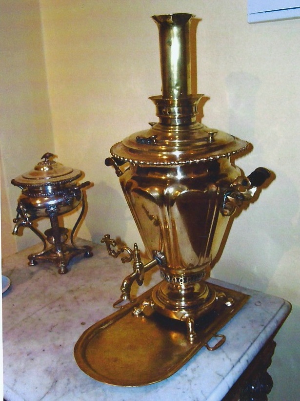 A gold samovar stands on a marble countertop next to a metal vessel on legs.