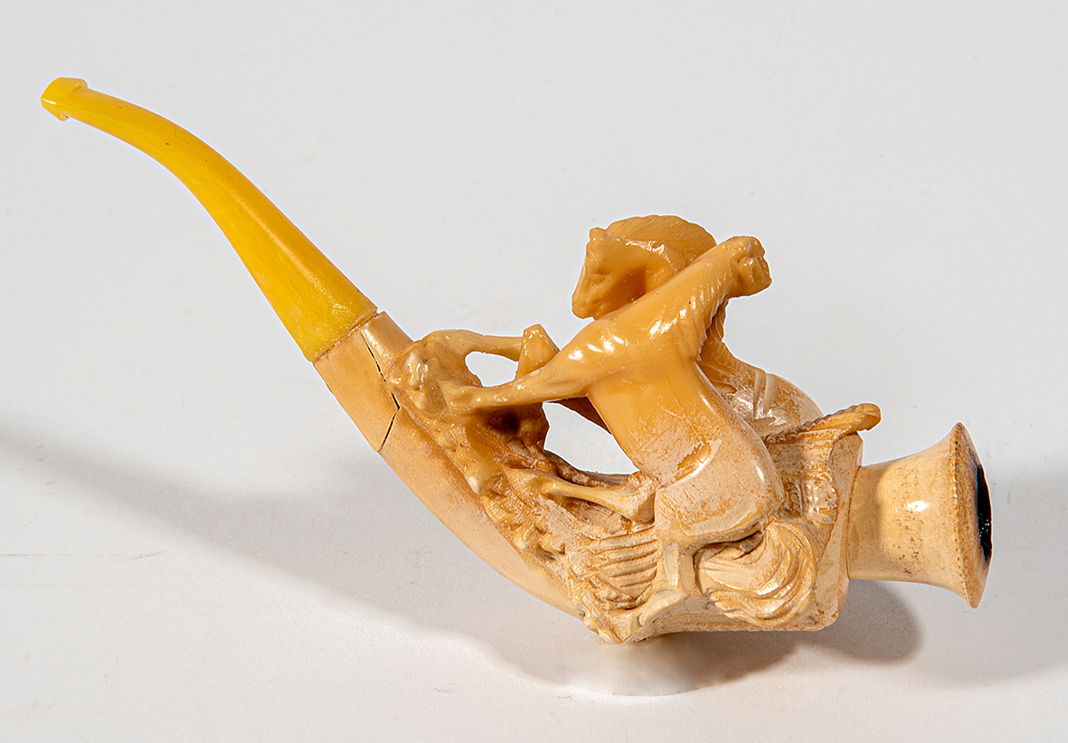 A carved pipe with an amber mouthpiece depicting a scene with a rider on a horse.