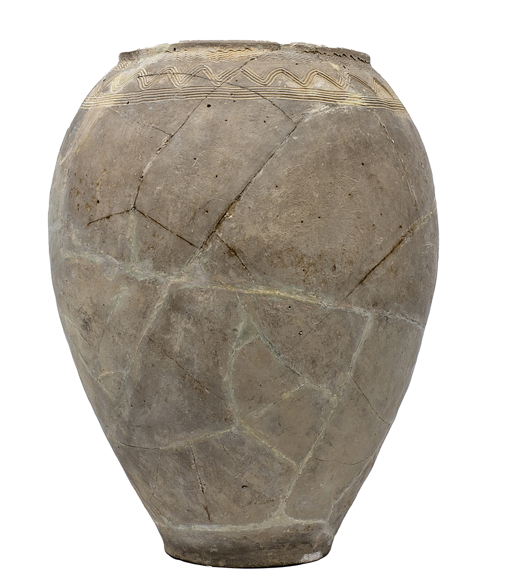 A large clay vessel with visible traces of reconstruction, decorated with a wavy pattern on the upper part.