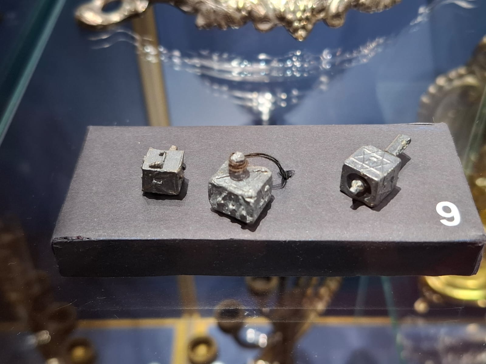 Three small, metal Hanukkah spinning tops set on a black stand