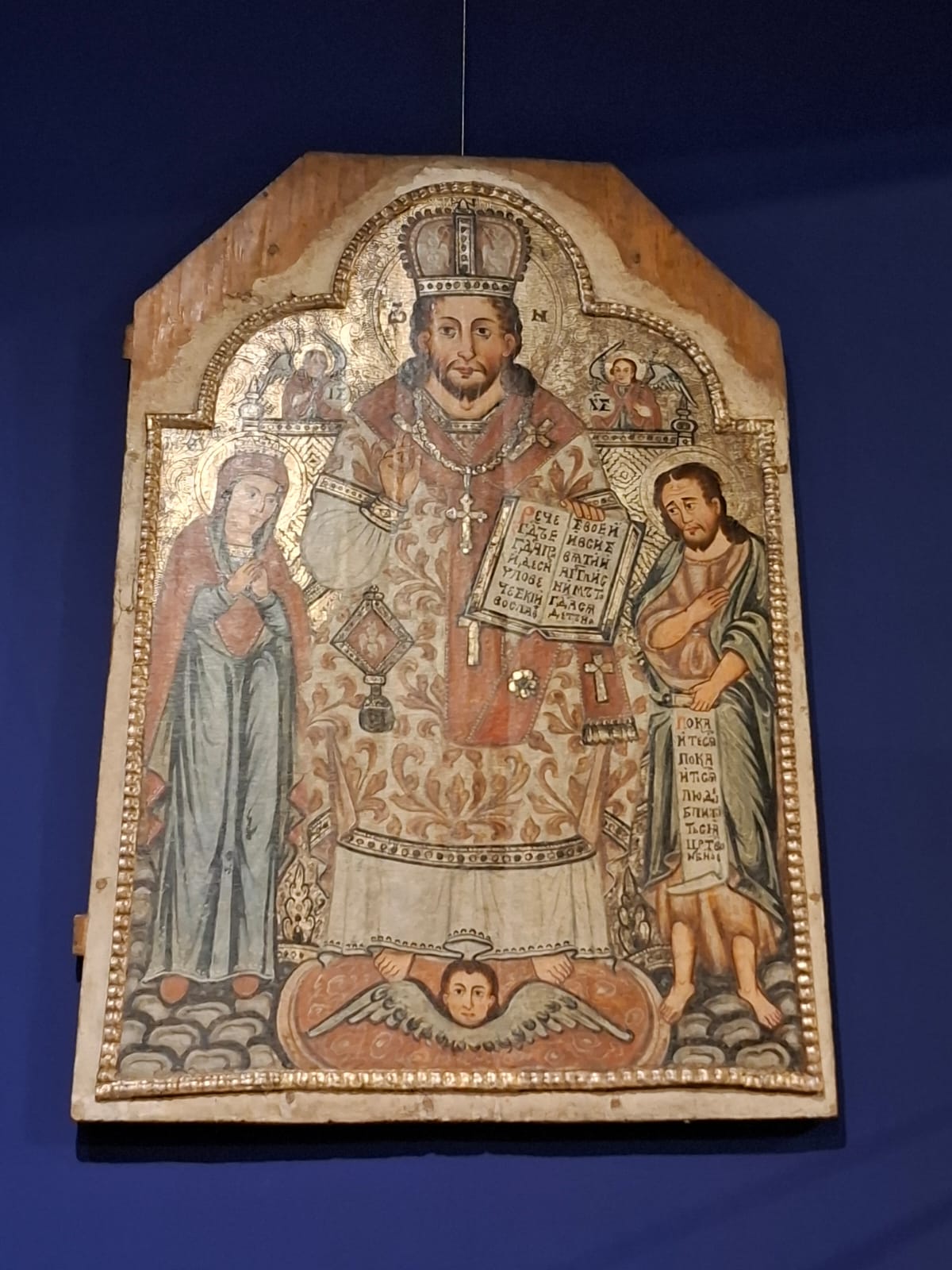 Religious icon depicting a bishop in liturgical vestments, flanked by saints, on a golden background.