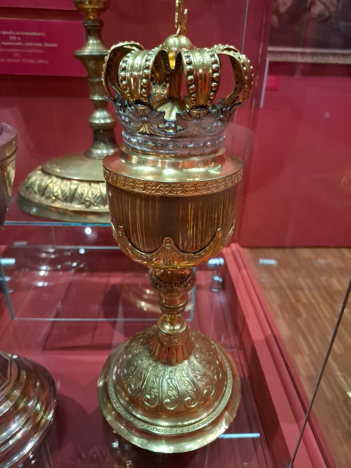 Srebrny kielich liturgiczny o bogato zdobionej podstawie i czaszy oraz korona o podobnym stylu, ustawione obok siebie.