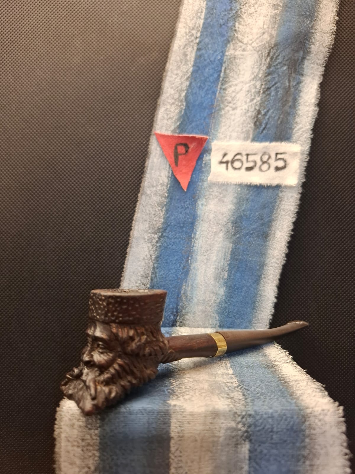 Rzeźbiona fajka z główką w kształcie brodatej twarzy mężczyzny, prezentowana w muzealnej gablocie.