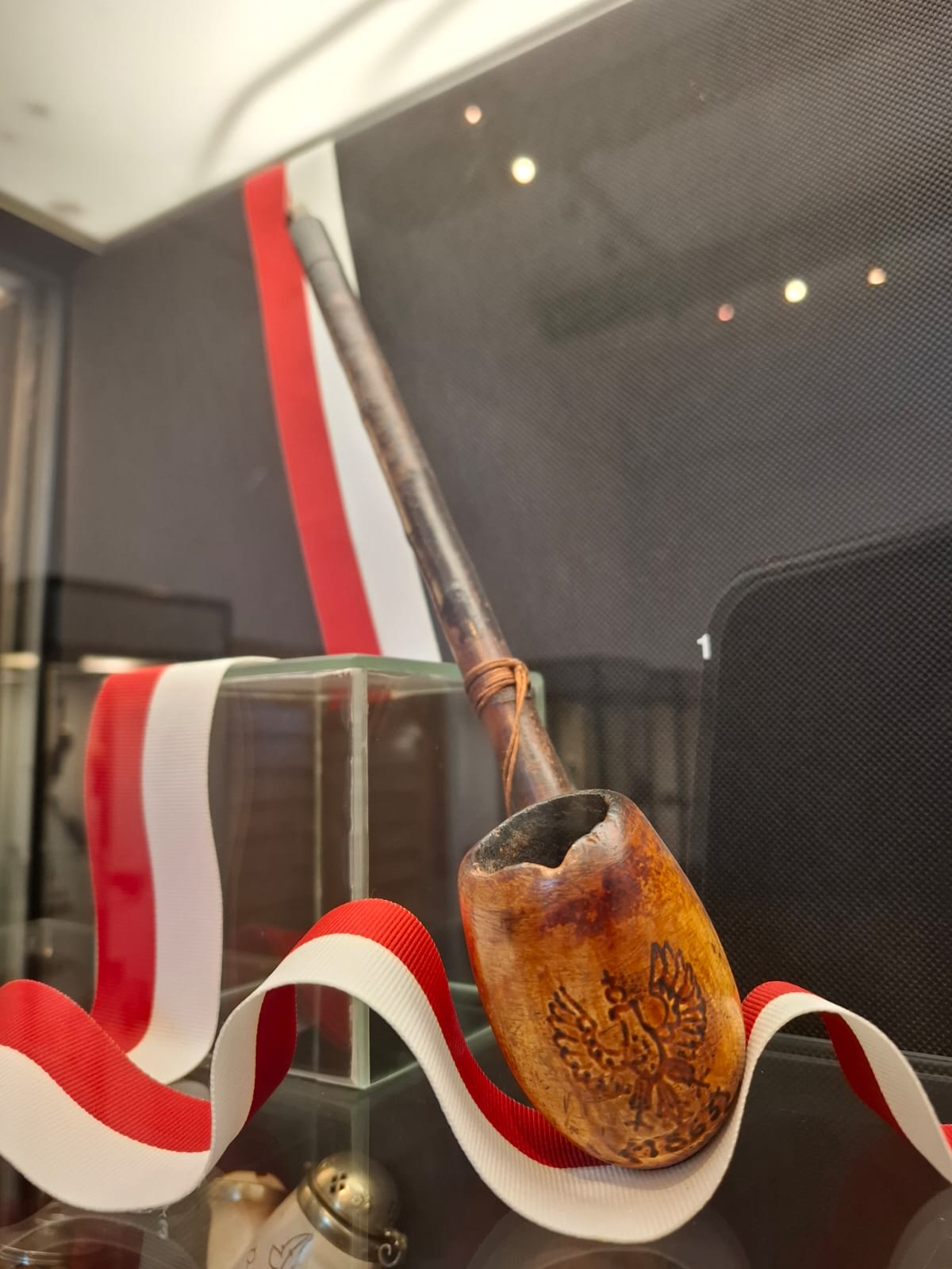 A wooden pipe with a long stem and an engraved eagle, decorated with a red and white ribbon.