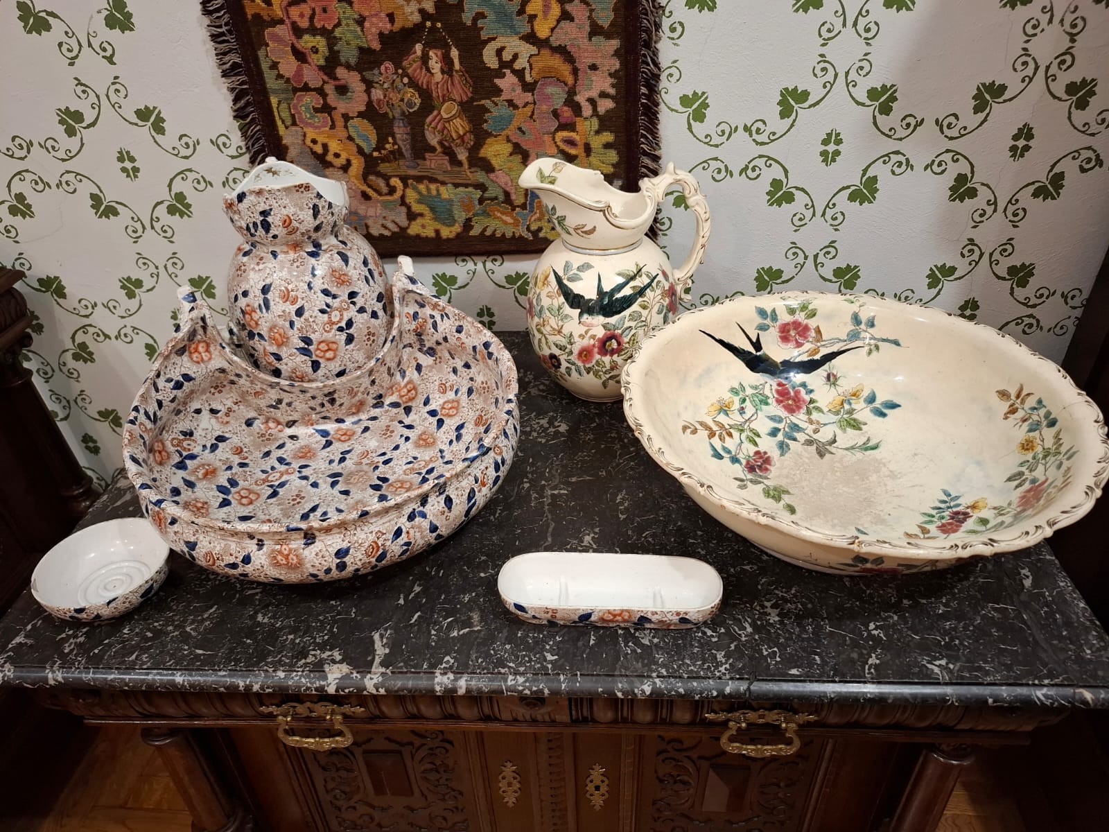 A set of decorated ceramics: a bowl, a jug and dishes, set on a marble countertop.
